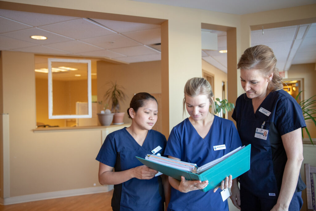 A group of Nursing students confer over a binder.