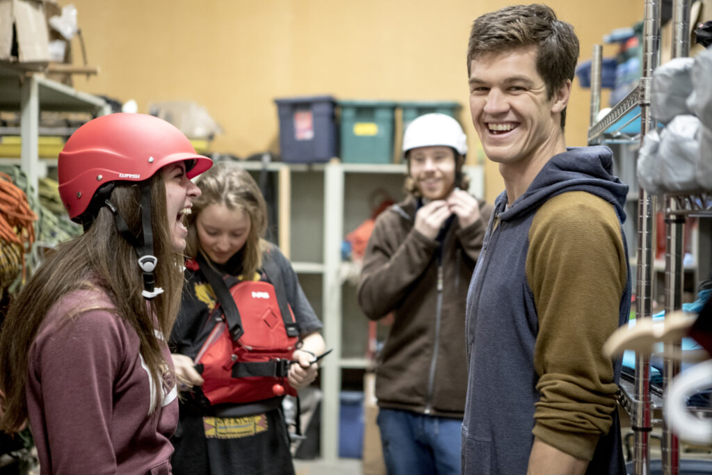 A group of Adventure Study student laugh while putting on helmets and life jackets.
