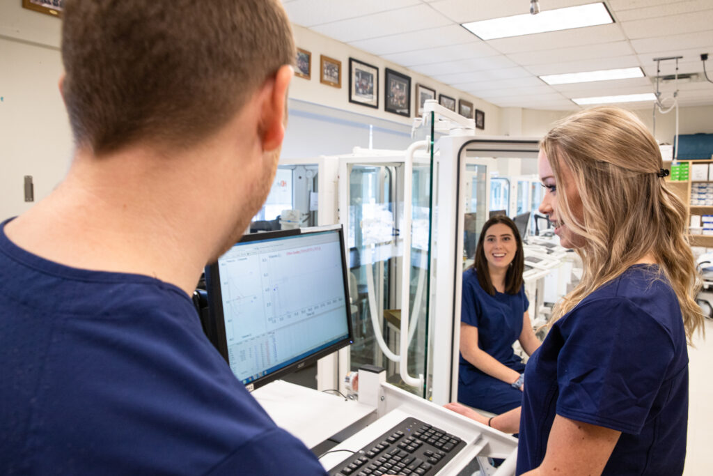 Three Respatory Therapy students talk while one student looks at a computer monitor.