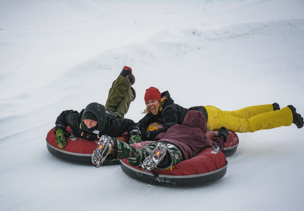 Three people slide down a a snowy hill on inner tubes.