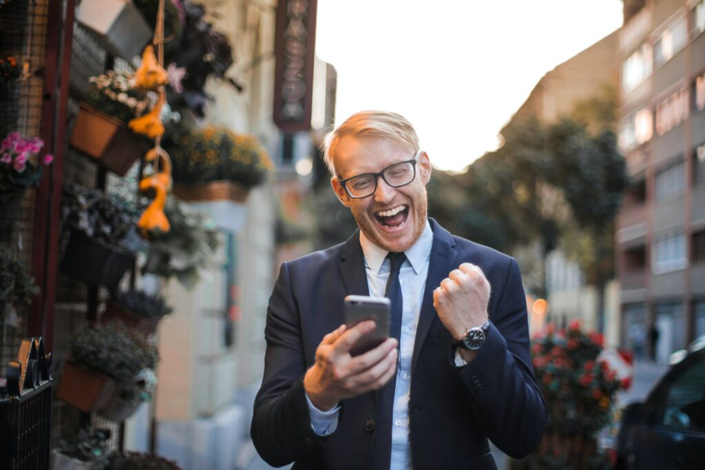 A man in a suit looks at his phone and celebrates.