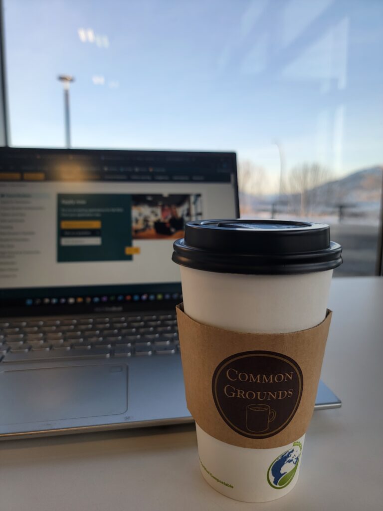Photo of a coffee from Common Grounds in front of an open laptop.