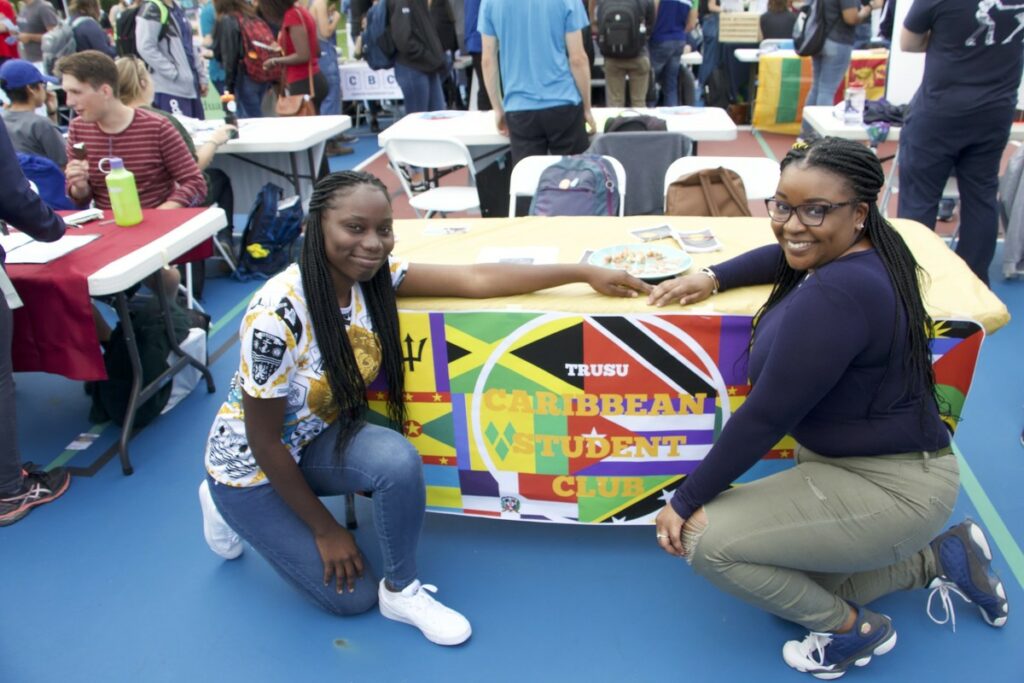Two students pose beside a banner that reads "TRUSU Caribbean Student Club"