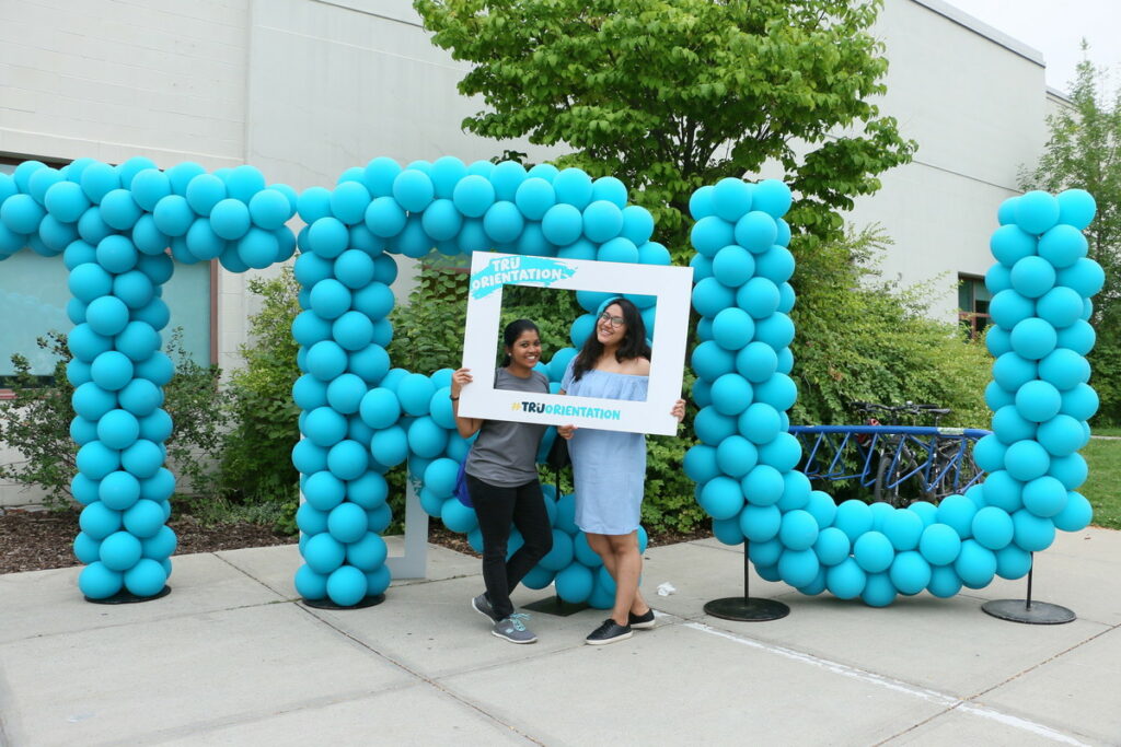 Two girls pose in front of balloons that spell "TRU".