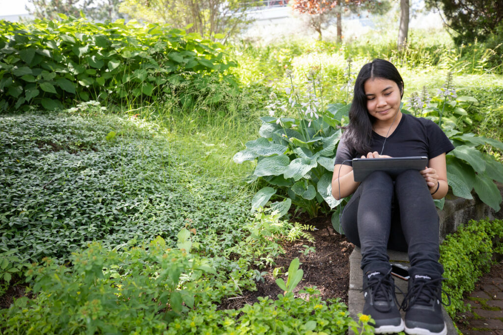 A student works on a tablet in the horticulture gardens.