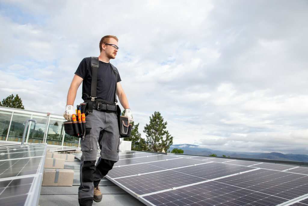A trades student walks between rows of solar panels on a roof.