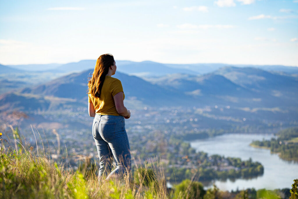A woman stands at the top of a hill on the Peterson creek hiking trail looking over the Thompson River and the valley.
